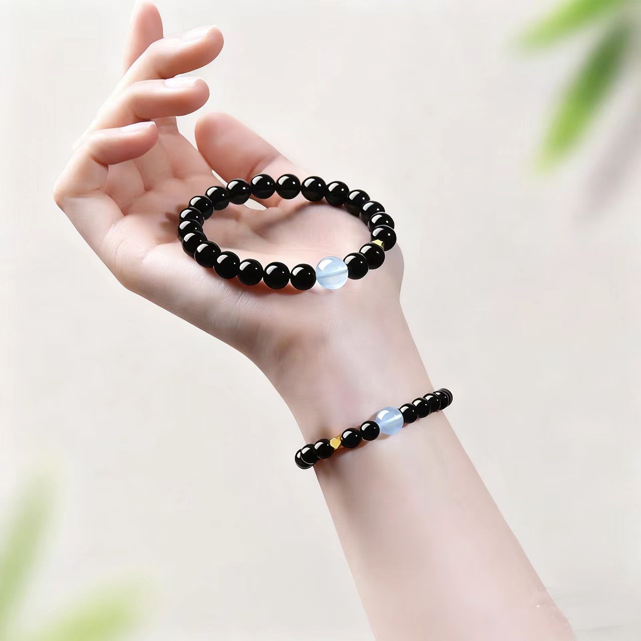 Hand wearing a black beaded bracelet on a light background