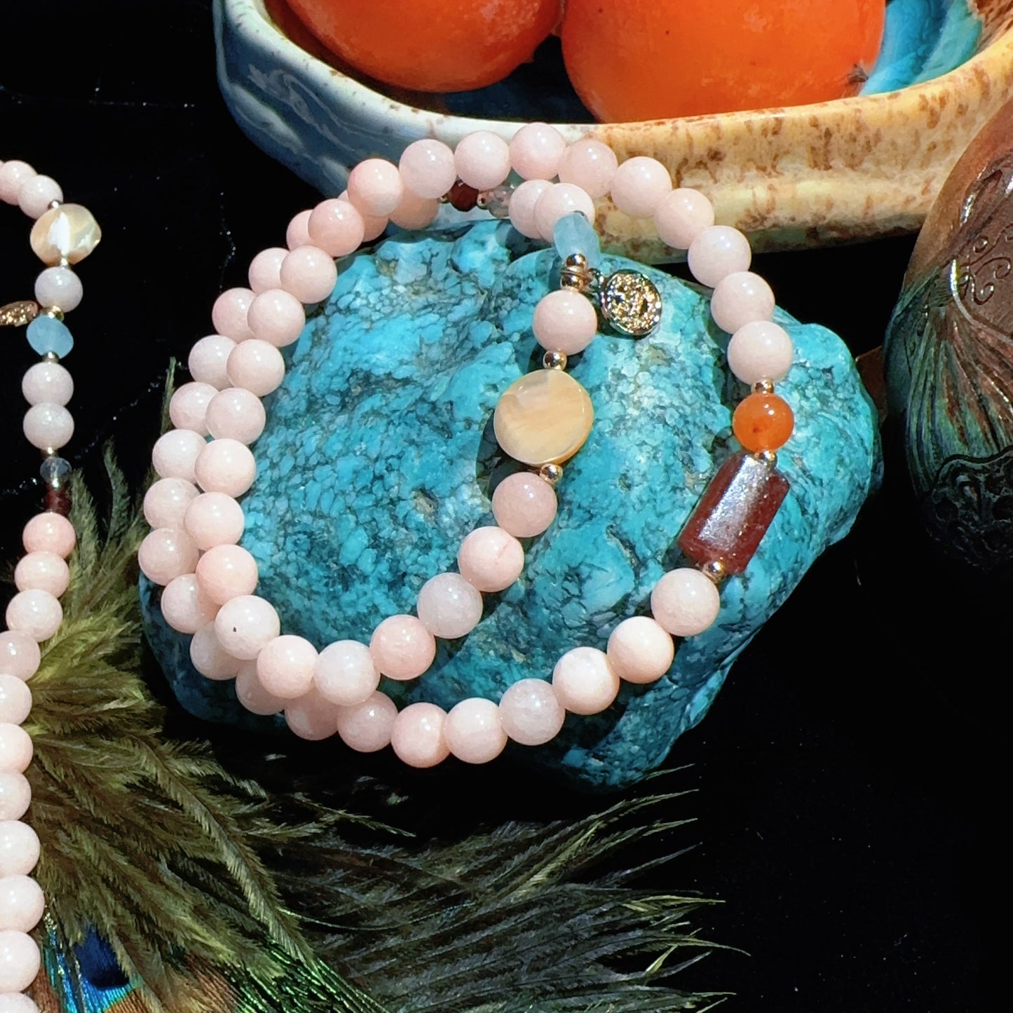 Necklace with pink beads on a turquoise stone with peaches in the background