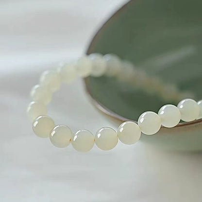 White beaded bracelet on a white surface with a blurred green object in the background