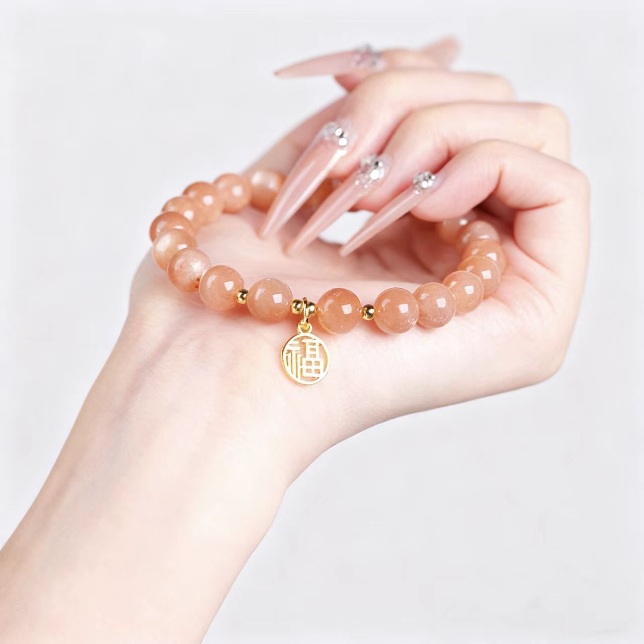 Hand wearing a peach-colored beaded bracelet with a gold charm on a light gray background