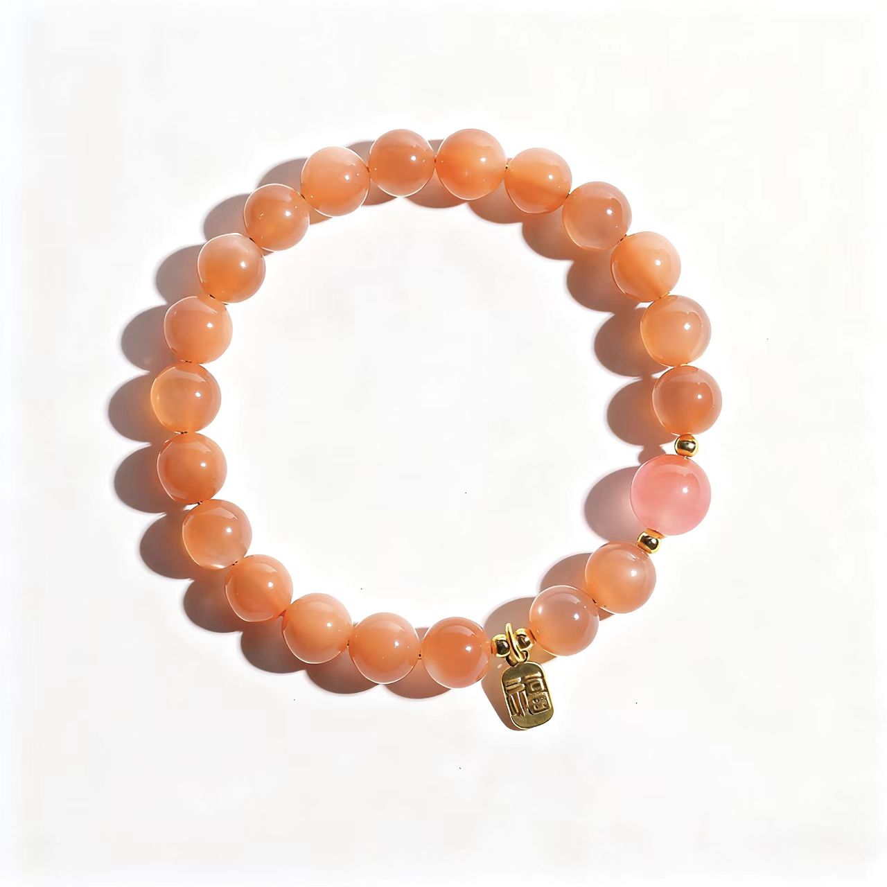 Peach-colored beaded bracelet with a gold charm on a white background