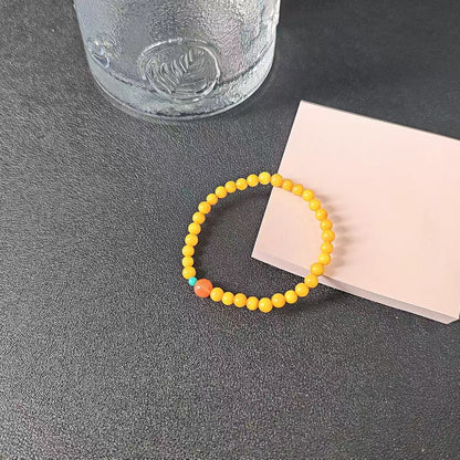 Yellow beaded bracelet on a dark surface with a glass and pink book