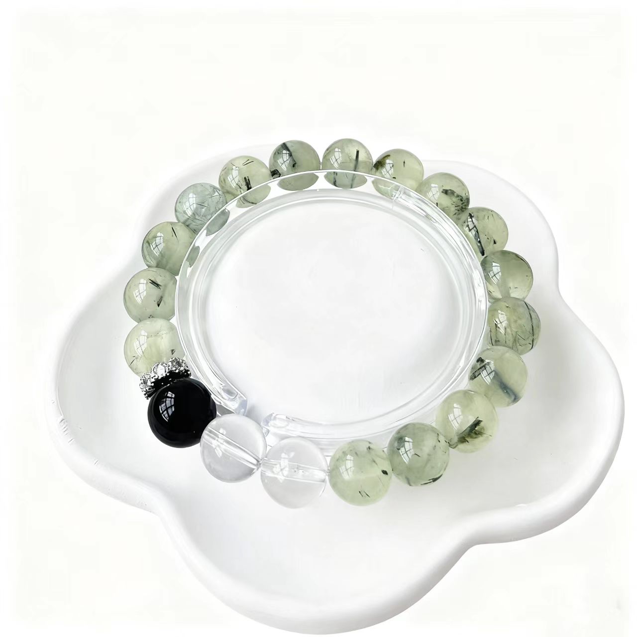 Green beaded bracelet with a black bead on a white dish