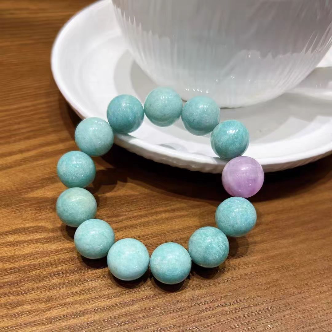 Turquoise beaded bracelet with a pink bead on a wooden surface with a white cup in the background.