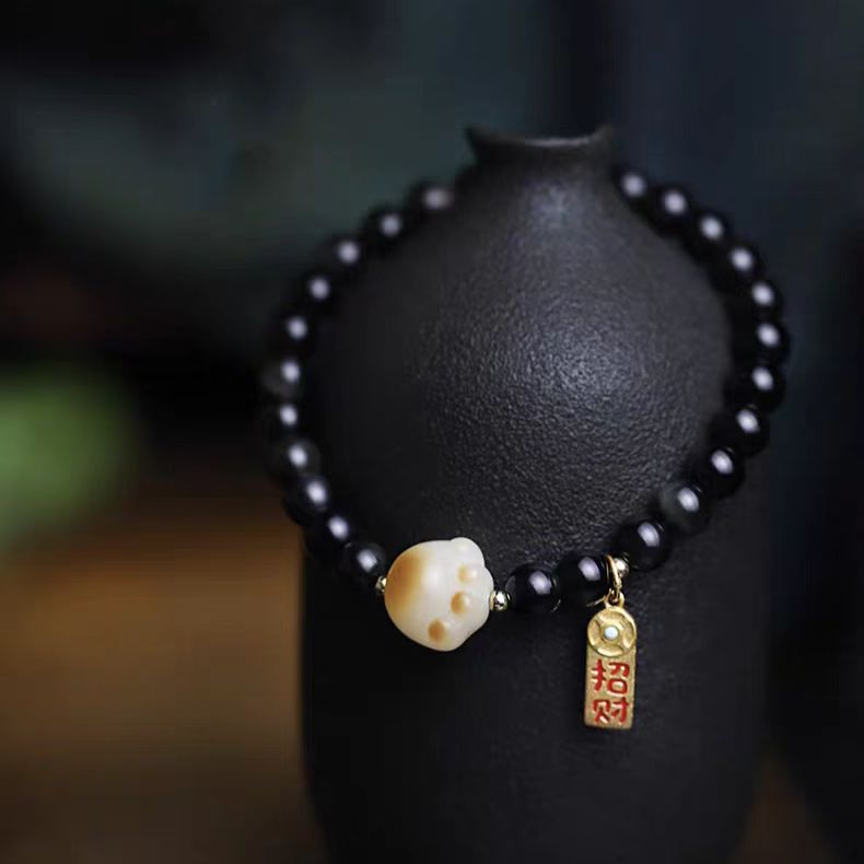 Black beaded bracelet with a gold charm on a dark background