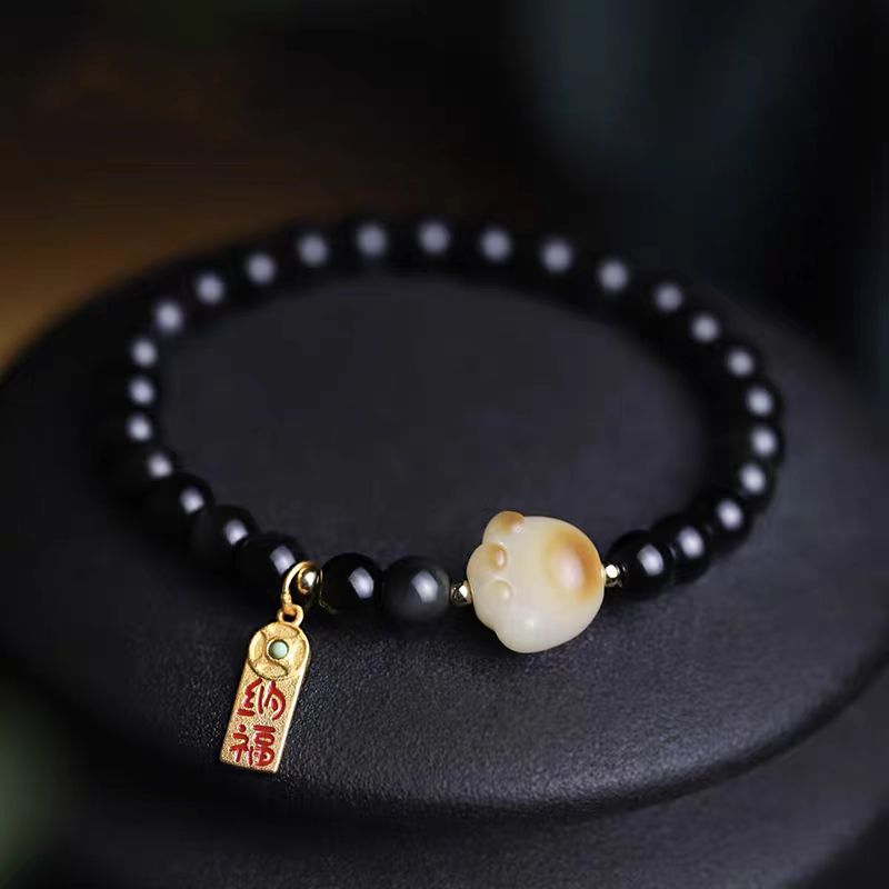 Black beaded bracelet with a gold and white charm on a dark surface