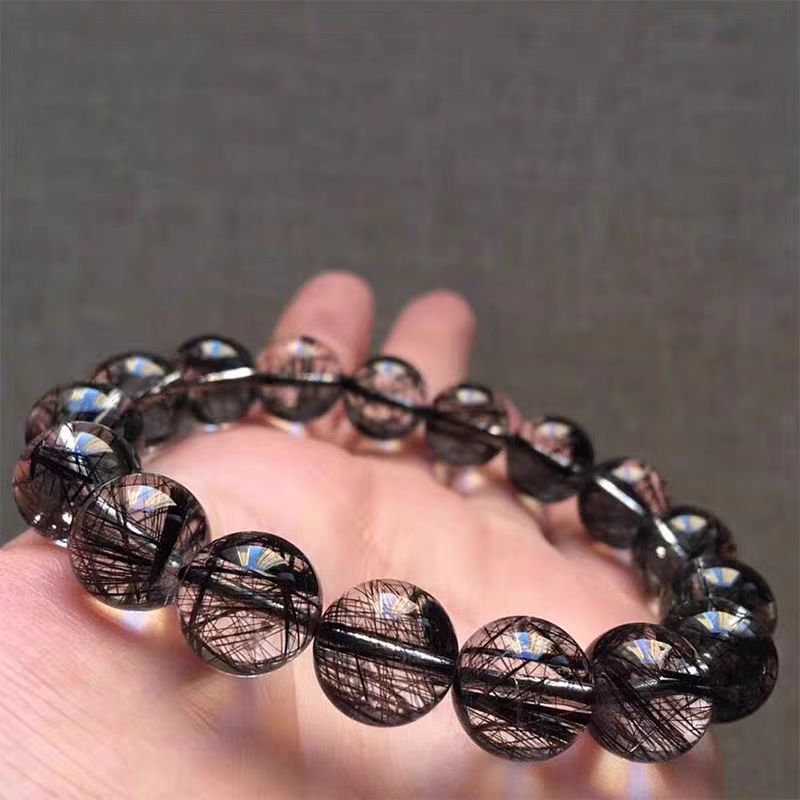 Bracelet with dark, textured beads on a hand against a gray background