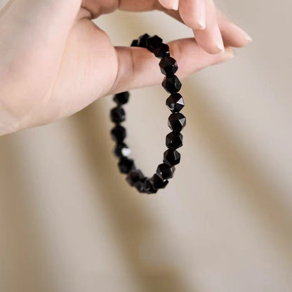 Black beaded bracelet held by a hand against a neutral background