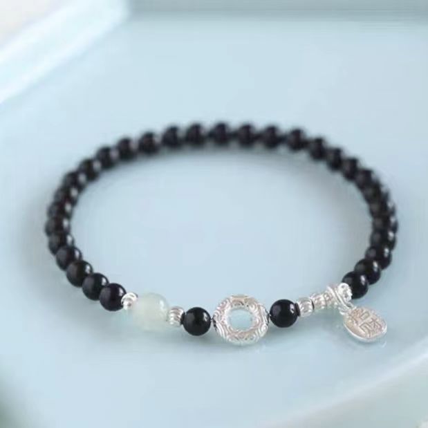 Black beaded bracelet with silver charm on a light blue background
