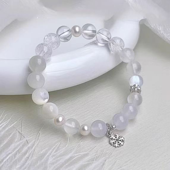 Beaded bracelet with pearls and a silver charm on a white surface