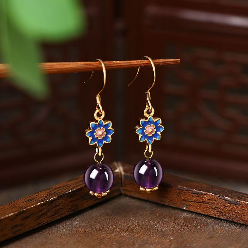 Pair of gold earrings with purple beads and blue flower designs on a wooden surface.