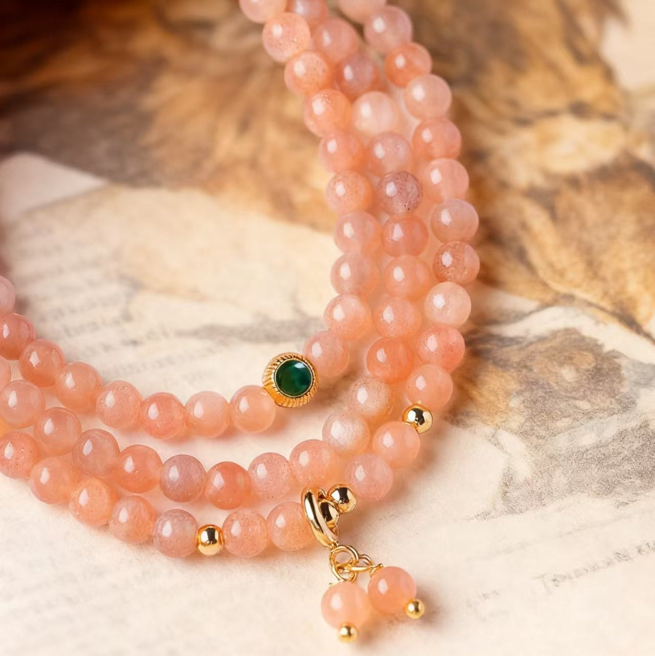 Stack of peach-colored beaded bracelets with gold accents on a marble surface.
