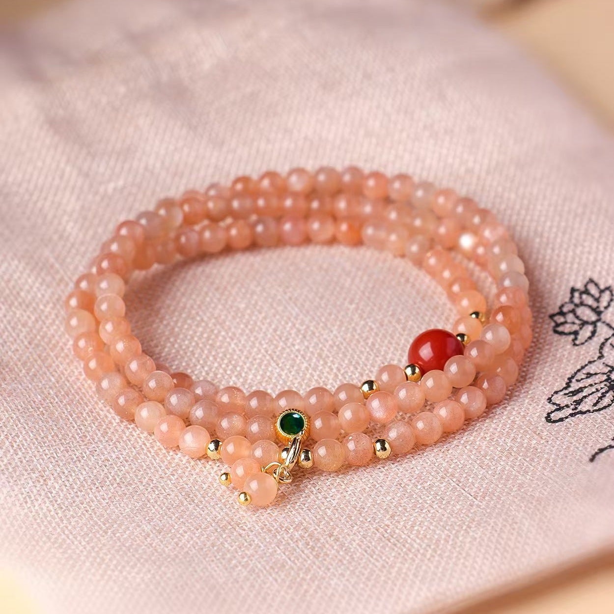 Pink beaded bracelet with green and red beads on a light pink fabric background