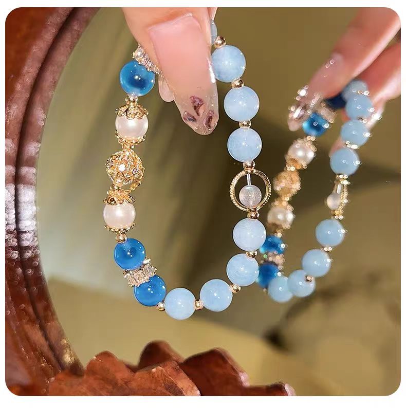 Beaded bracelet with blue and white beads held by a hand against a blurred natural background