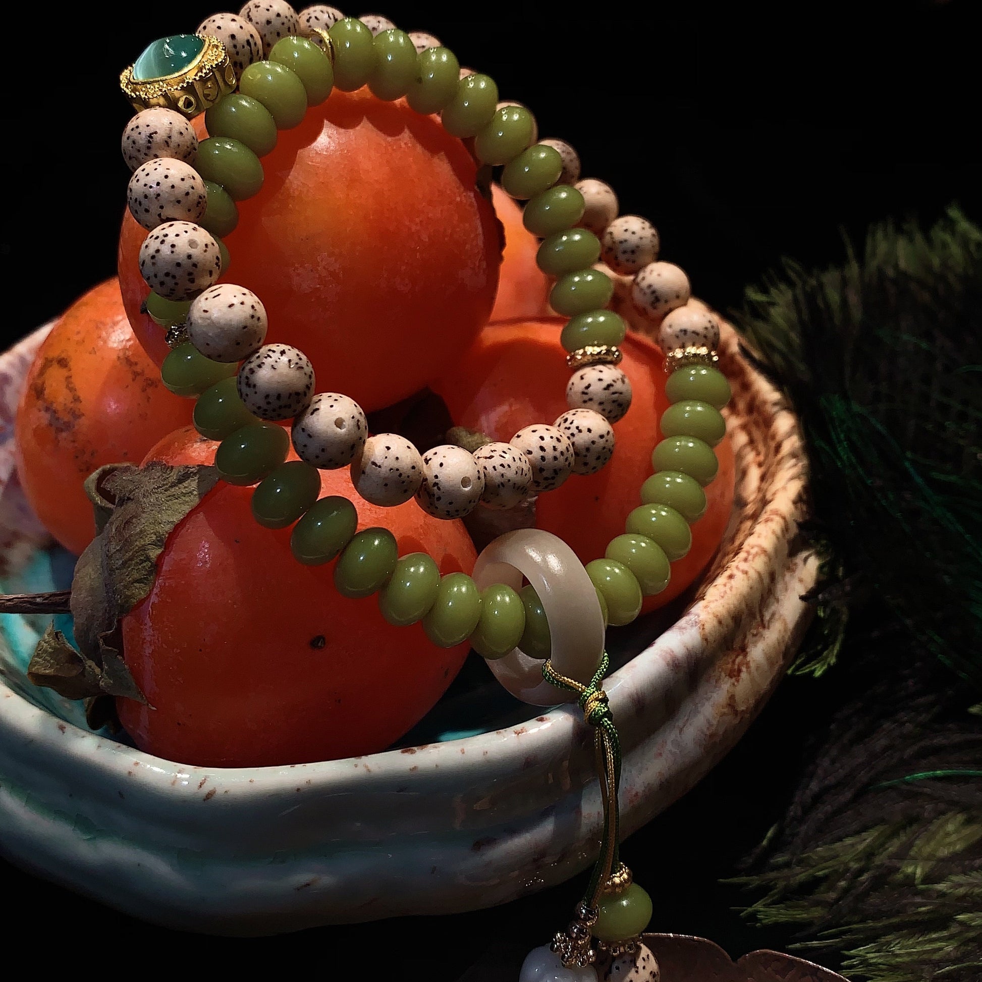 Green and white beaded bracelet on persimmons with a dark background