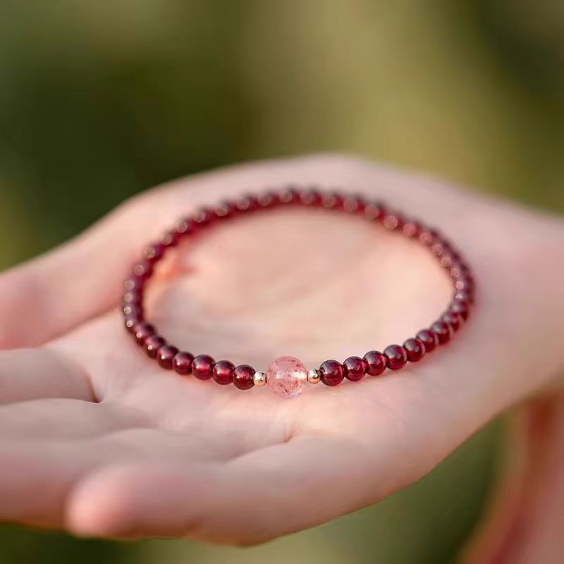 Garnet bracelet with a pink crystal held in a hand against a blurred green background