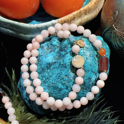 Necklace with white beads on a turquoise stone, surrounded by fruits and a teapot.
