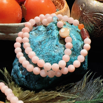 Pink beaded bracelet on a blue stone with peaches and a teapot in the background