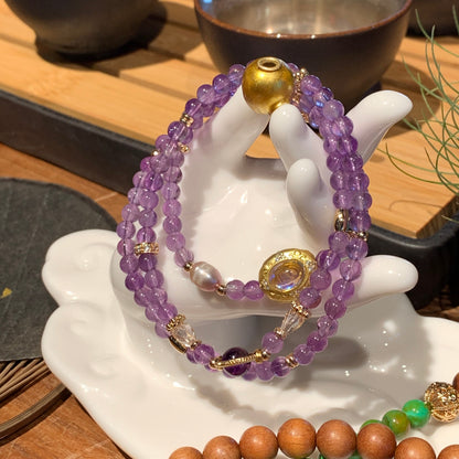 Amethyst beaded bracelet with gold accents on a white dish, with other bracelets in the background.