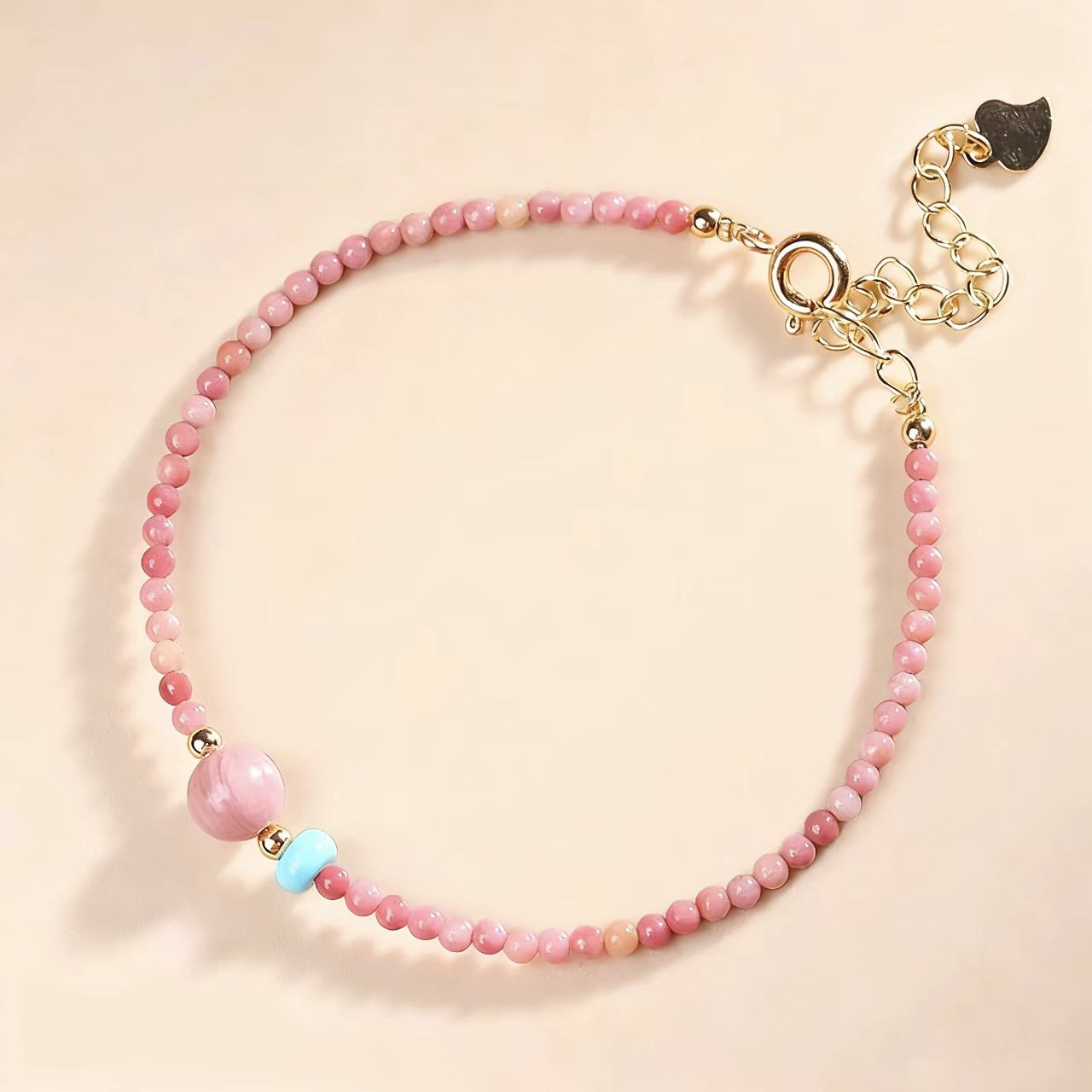Pink beaded bracelet with a gold clasp on a beige background